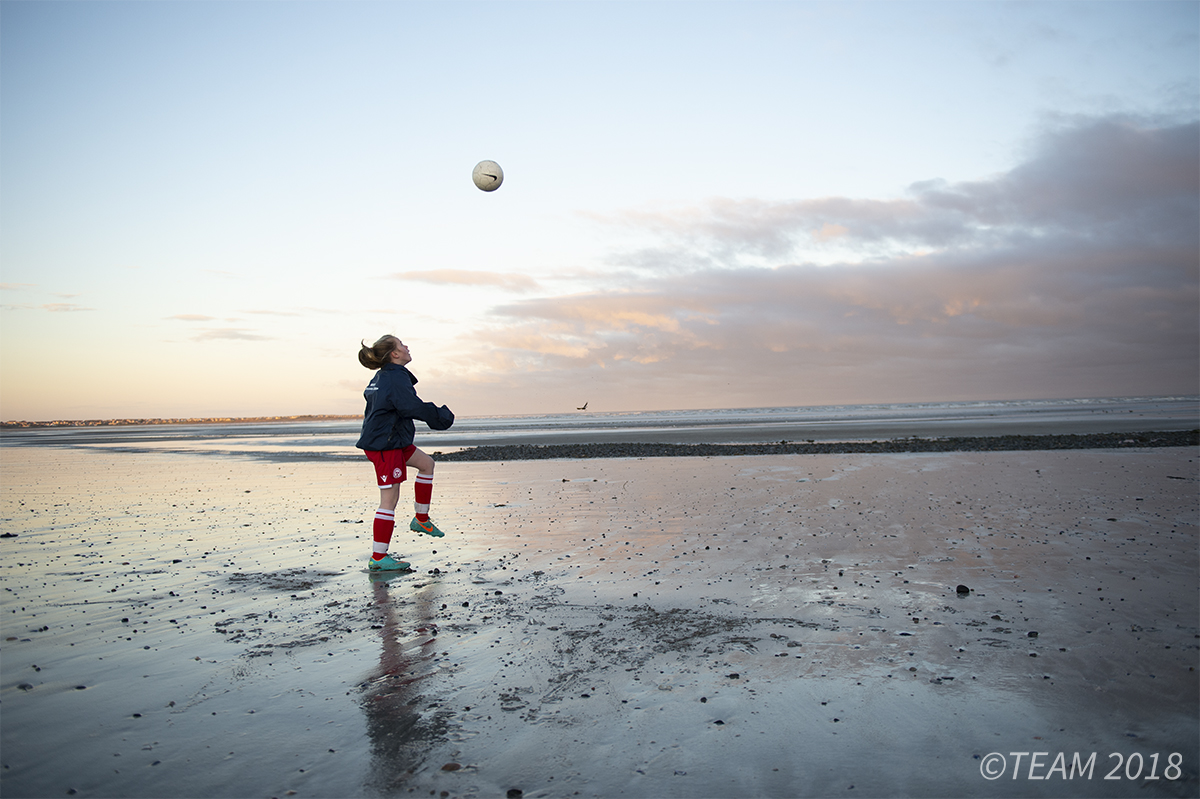 A girl plays with a soccer ball on the beach at sunset