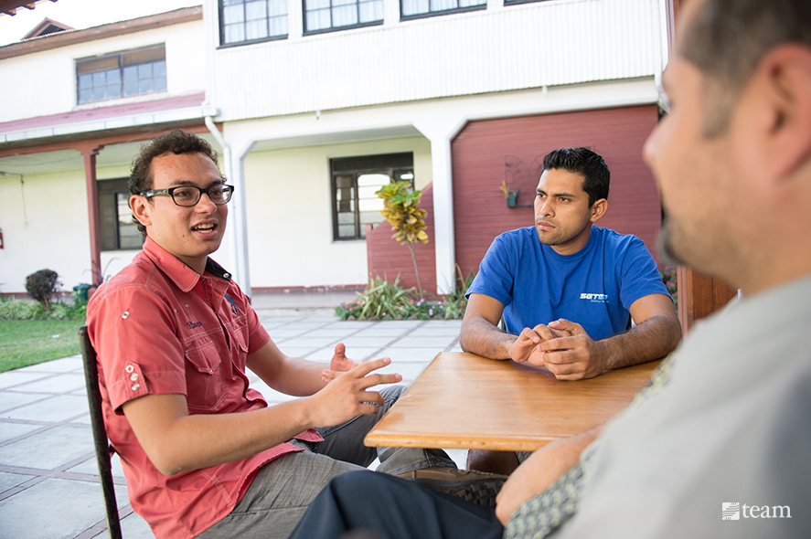 Three men talking around a table.