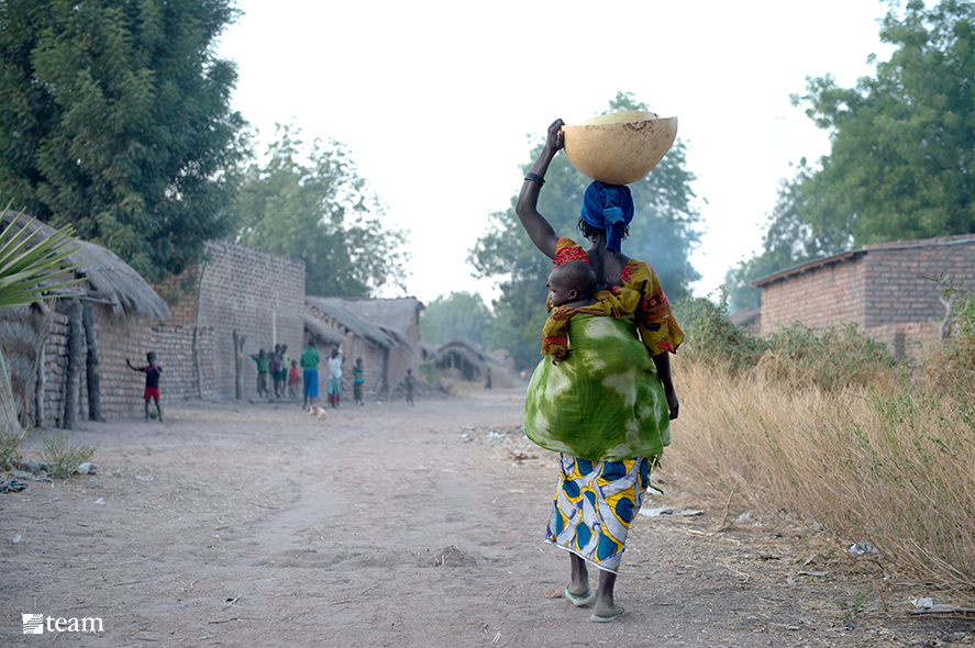 Chadian woman carrying water and baby on her back.