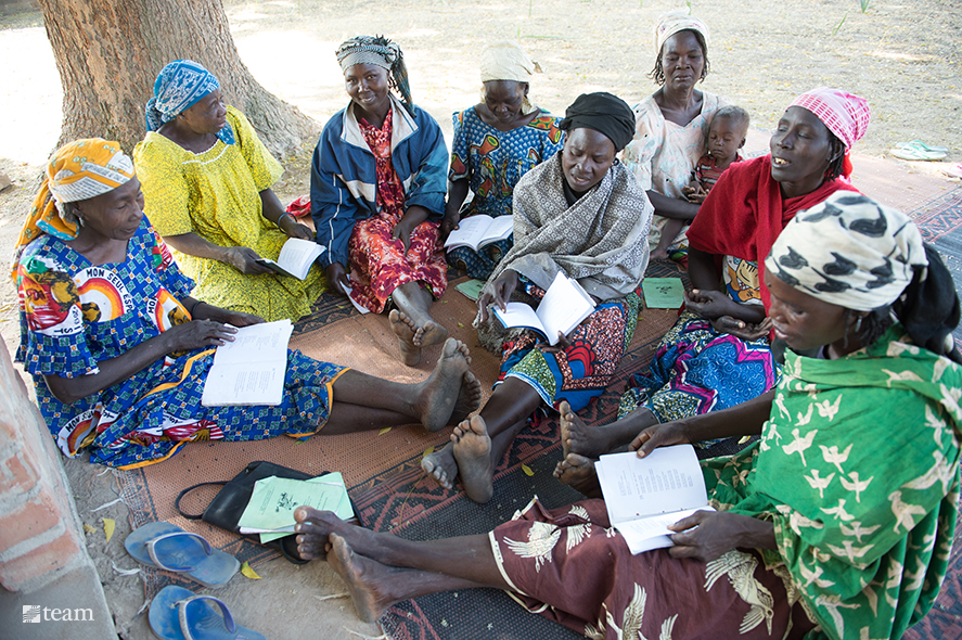 Several women sitting on a mat reading the Bible.