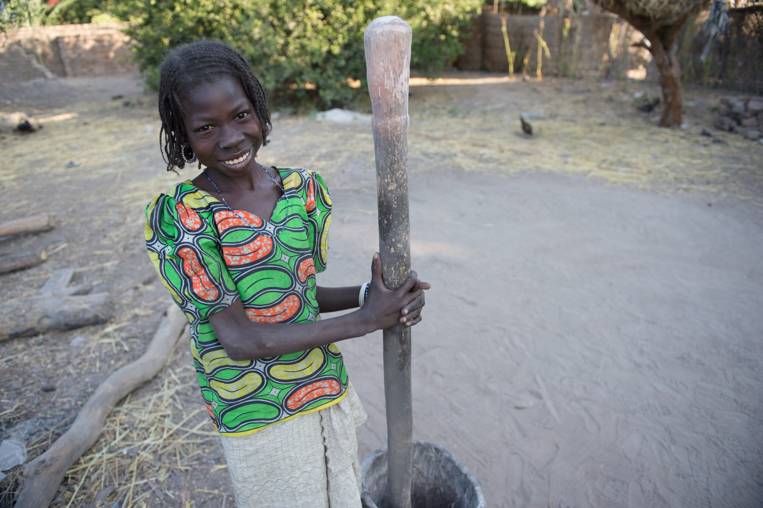 Young African girl grinding grain and smiling.