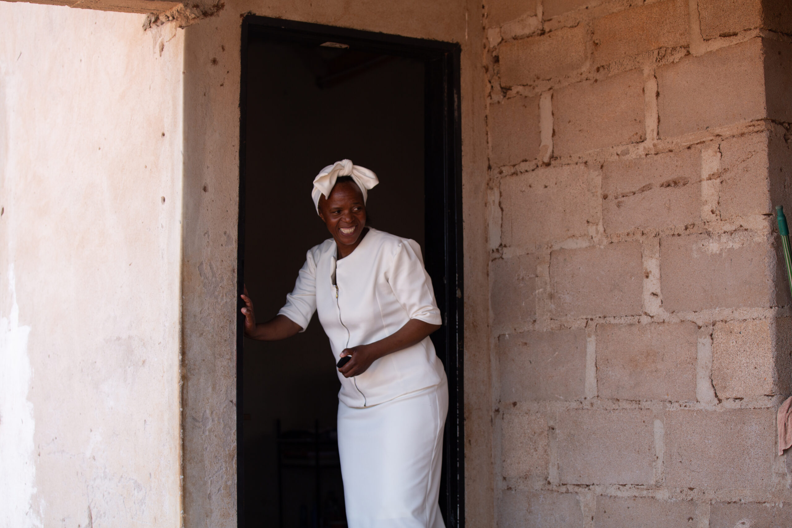 African woman standing in front of a doorway smiling.