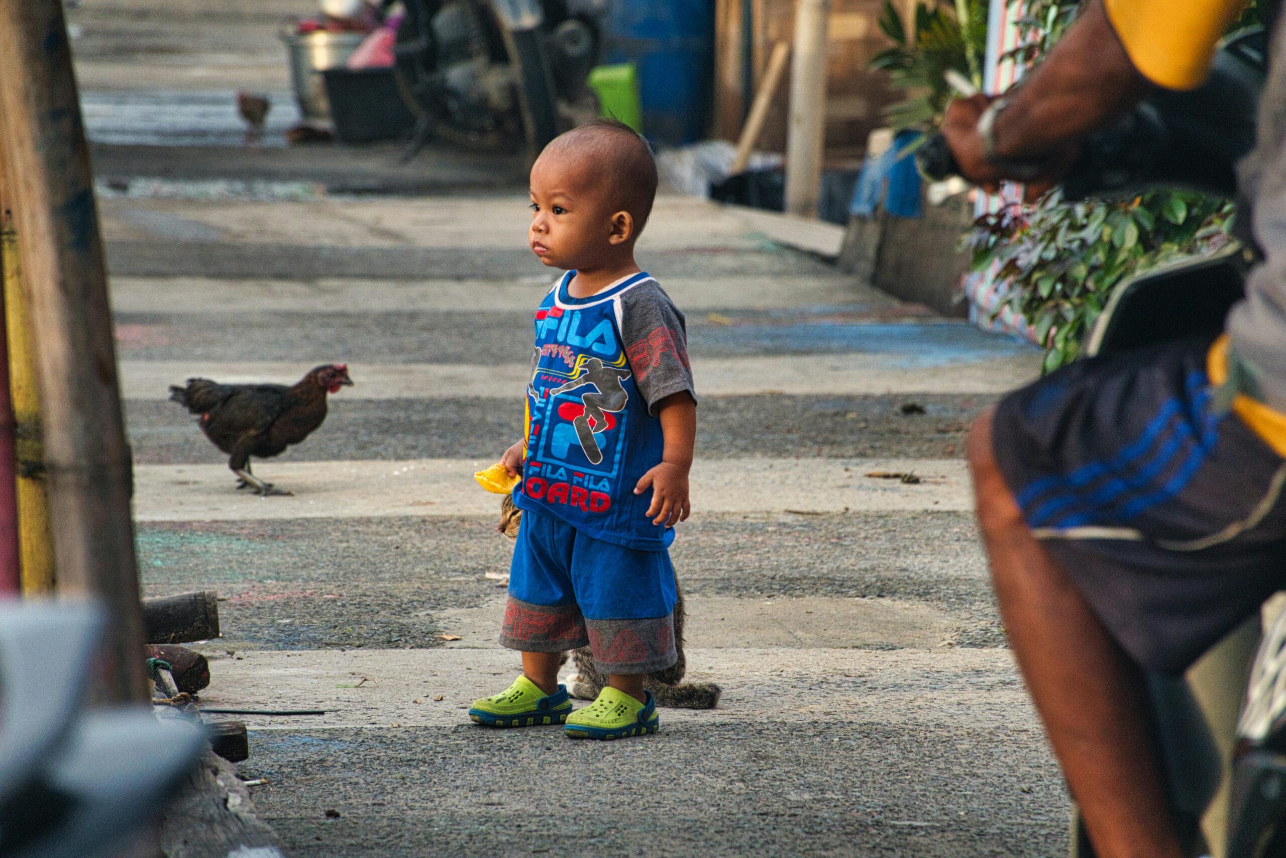 Toddler standing in the street with snack in hand.