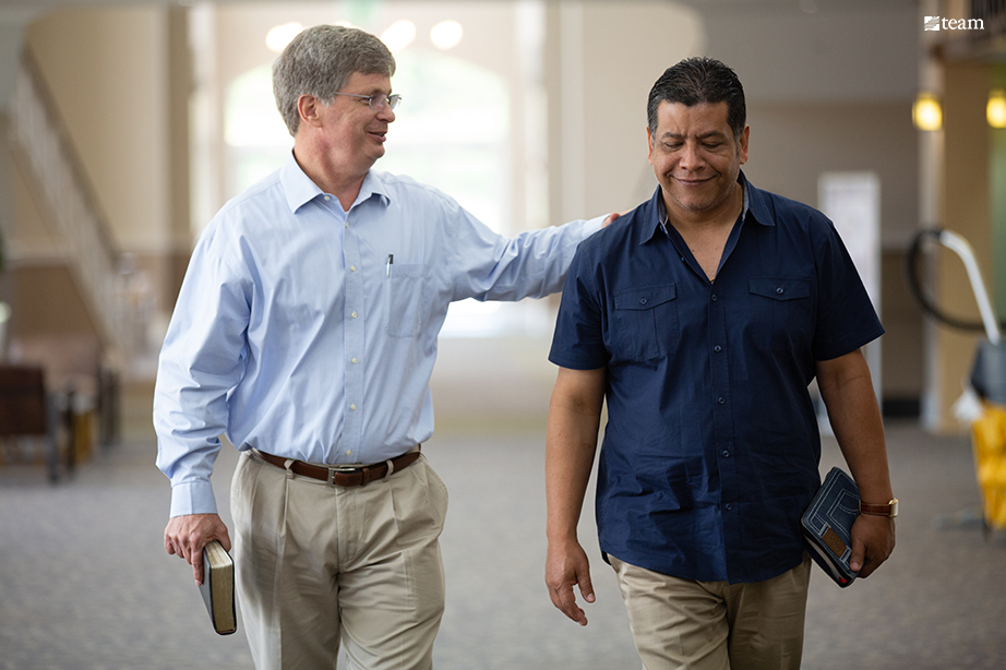 Two men walking beside one another and smiling.