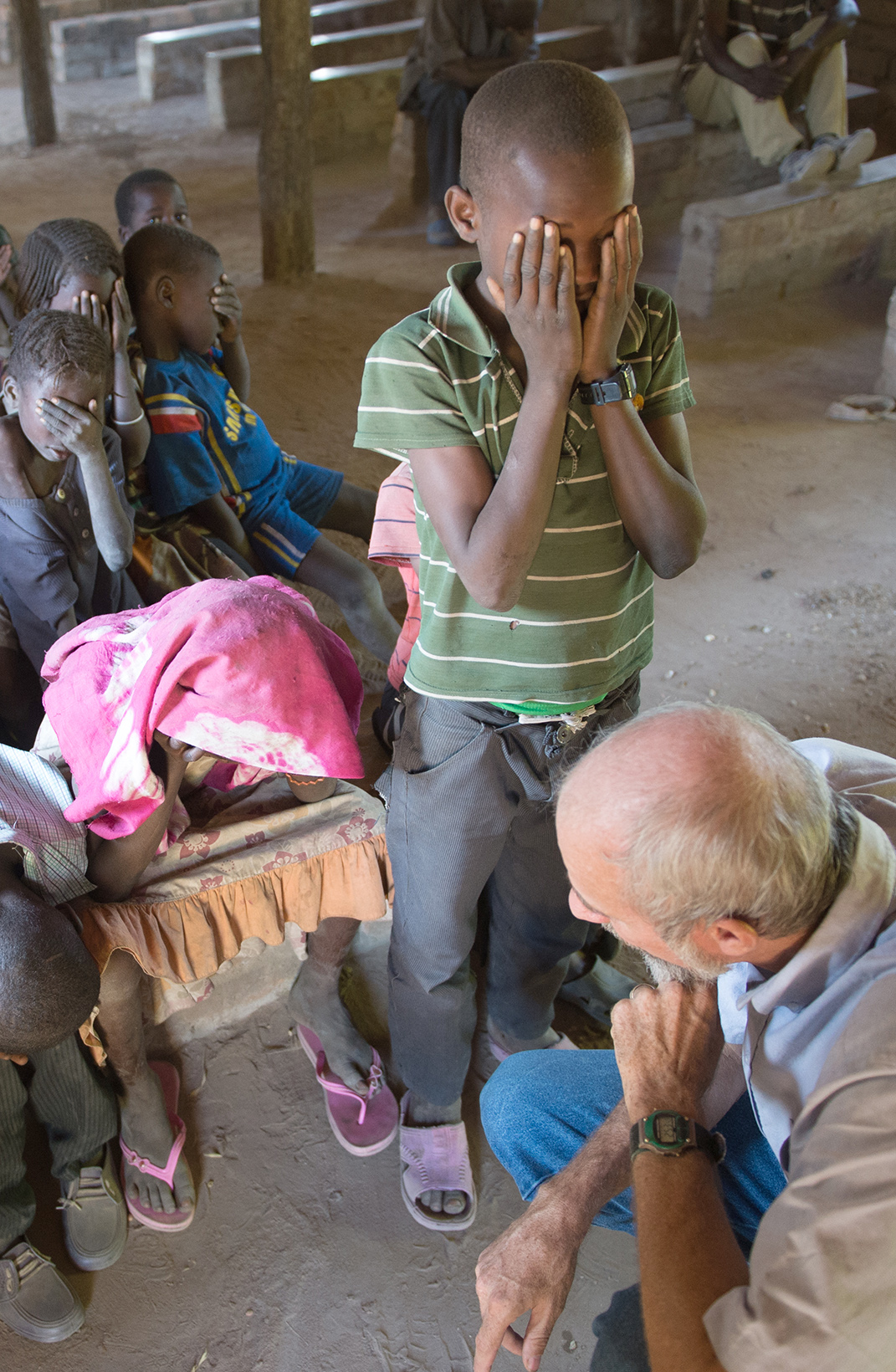 A group of children bow their heads praying with a boy standing in front.