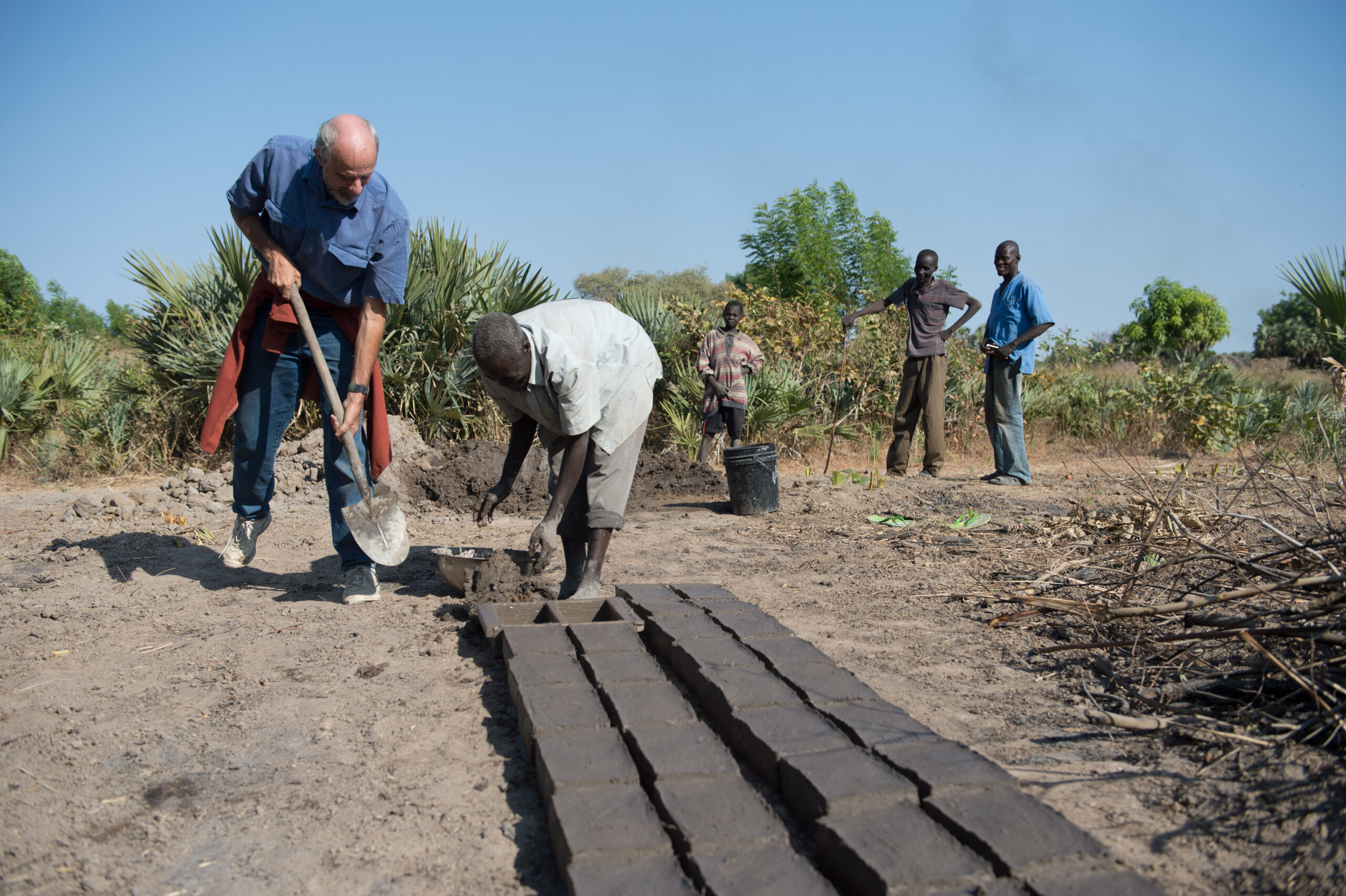 Two men shoveling mud to make bricks.