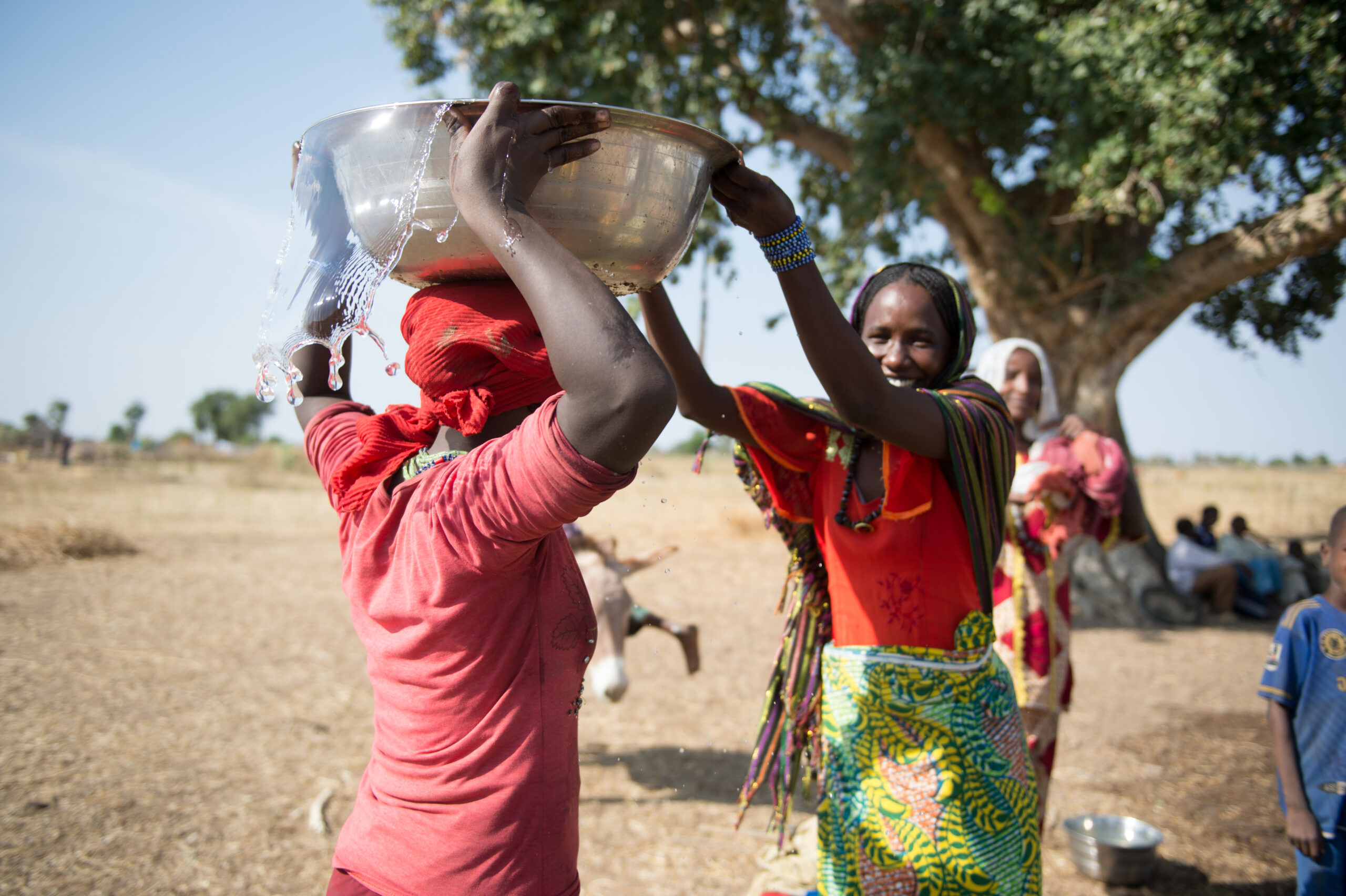 A woman putting a bowl of water on another woman's head to transport.