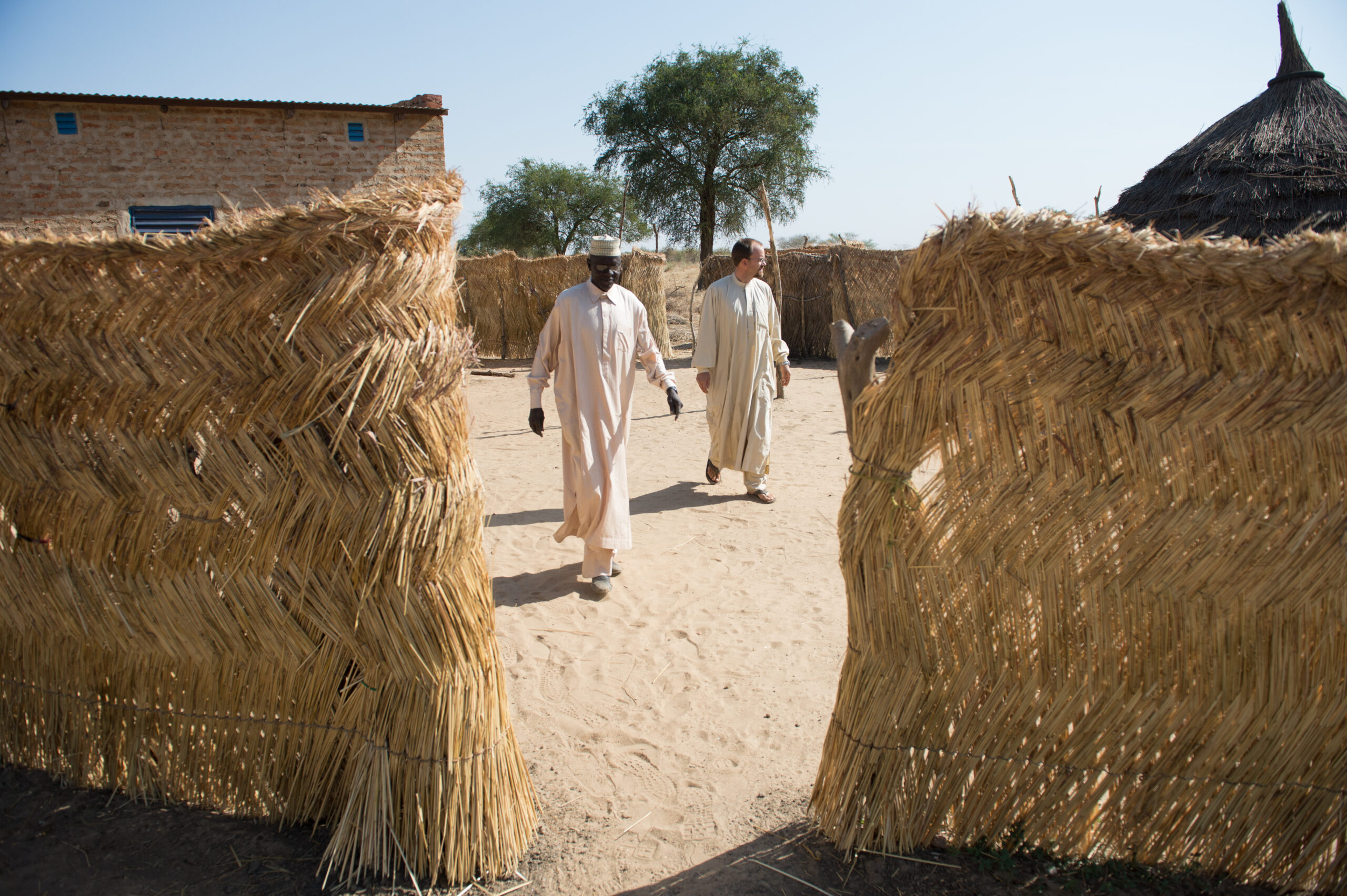 Two men walk between straw barriers.