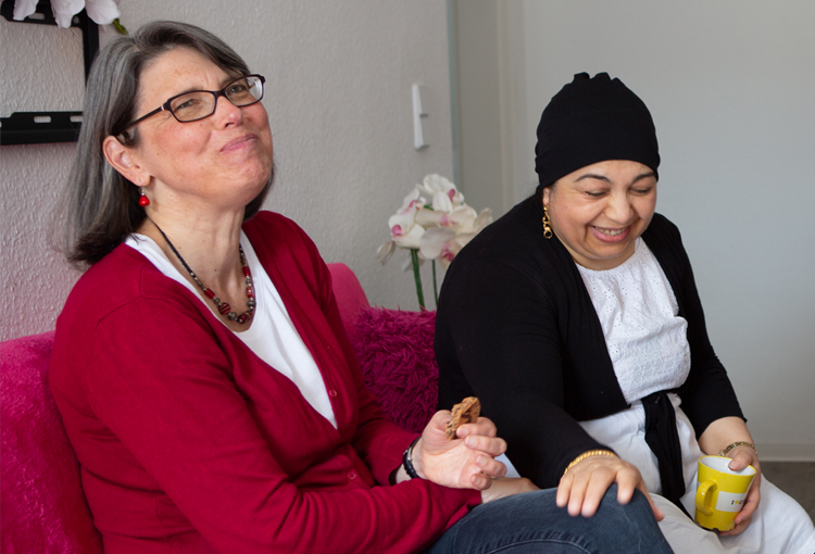 Two ladies sit laughing as they share cookies and tea.