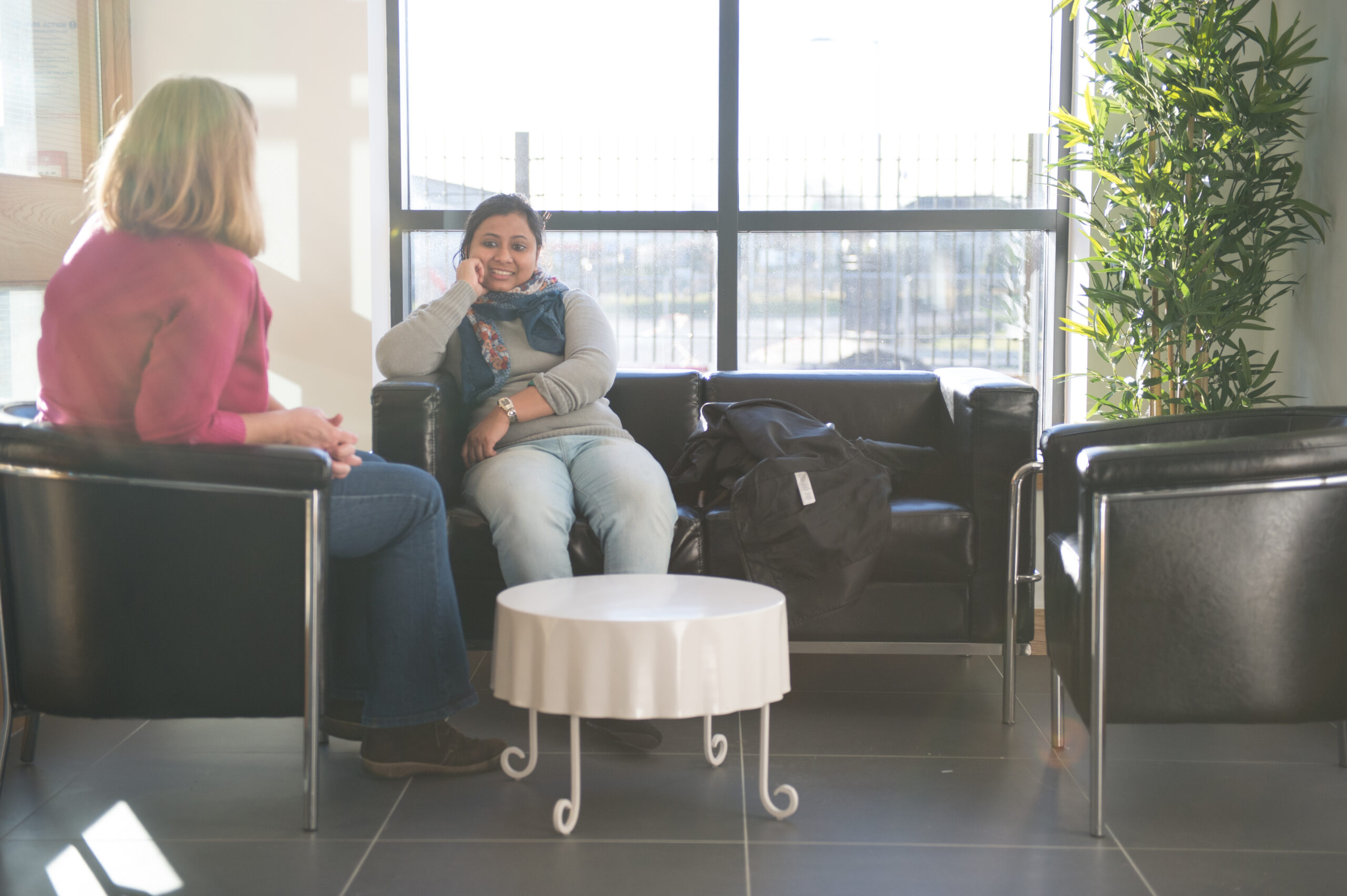 Two women sit on couches having a conversation.