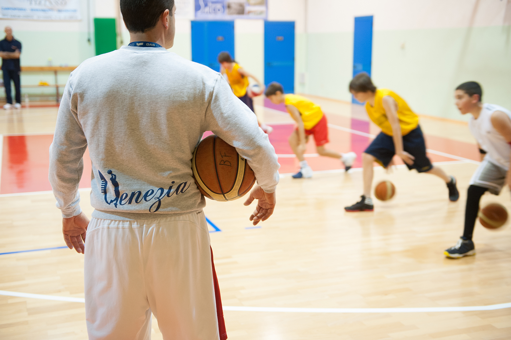 A coach stands and watches boys do basketball drills.