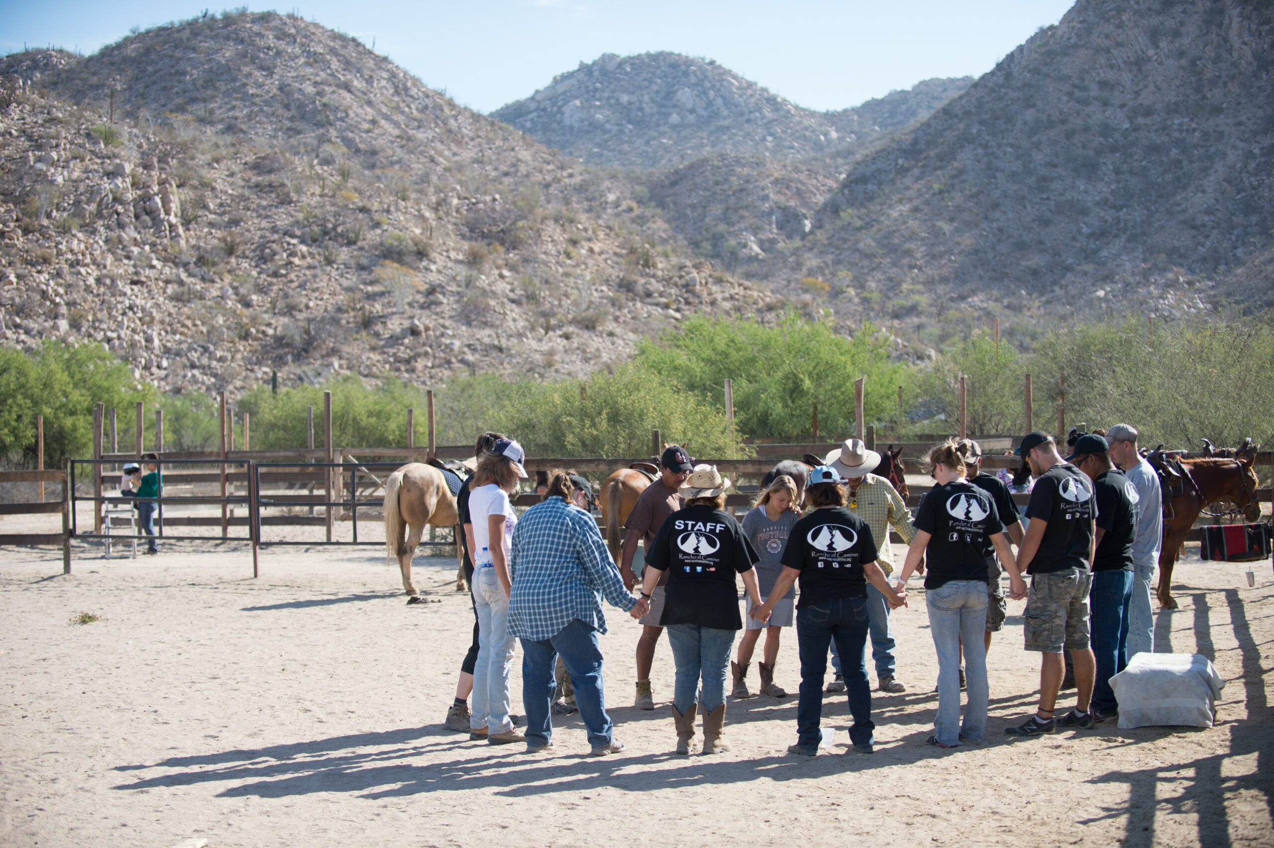 A group holding hands in a circle praying on a ranch.