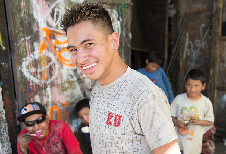 A young adult man stands smiling with a group a boys behind him.