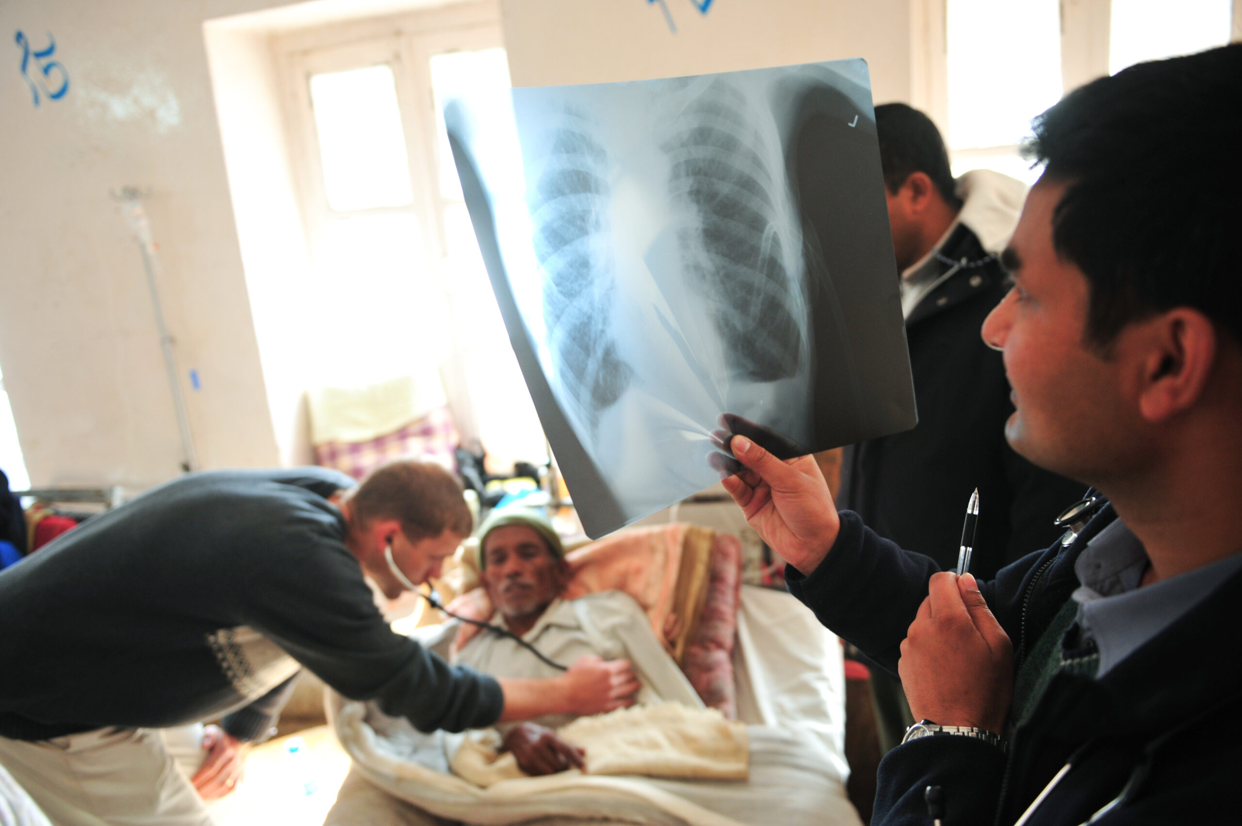 A doctor looks at a chest x-ray next to the patient in bed.