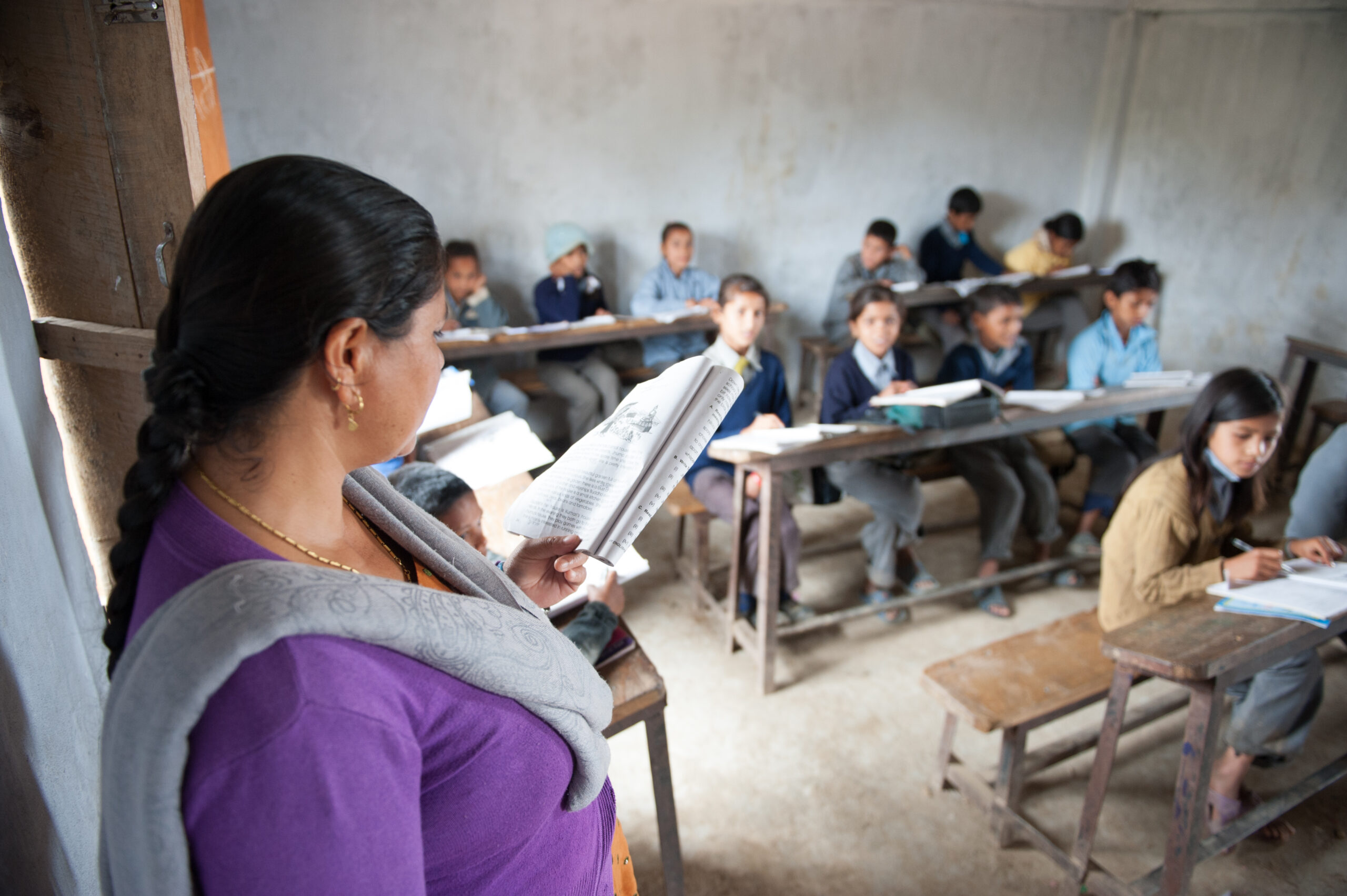 A teacher standing in front of her class reading from a booklet.