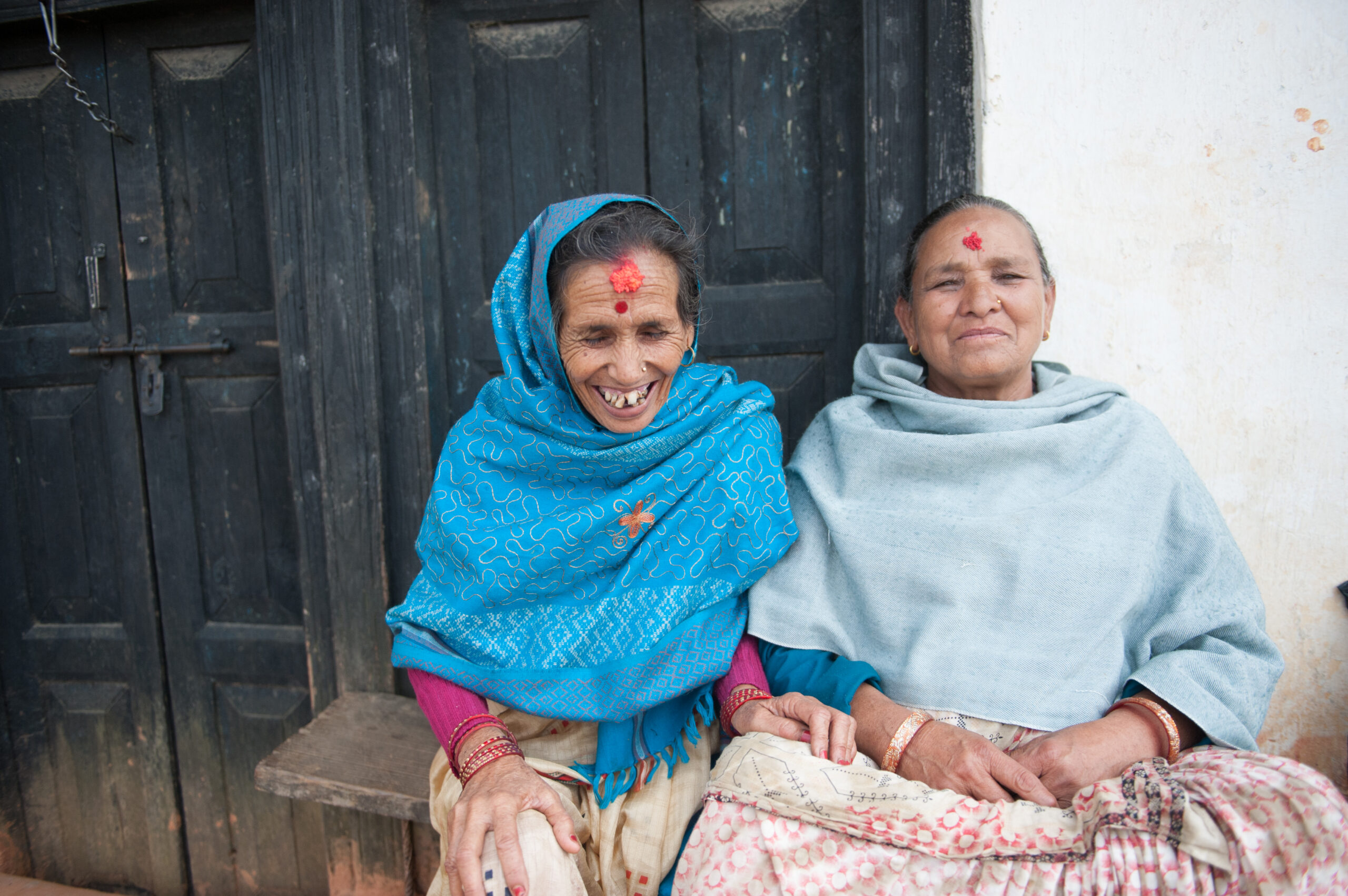 Two ladies sit on a bench laughing together.