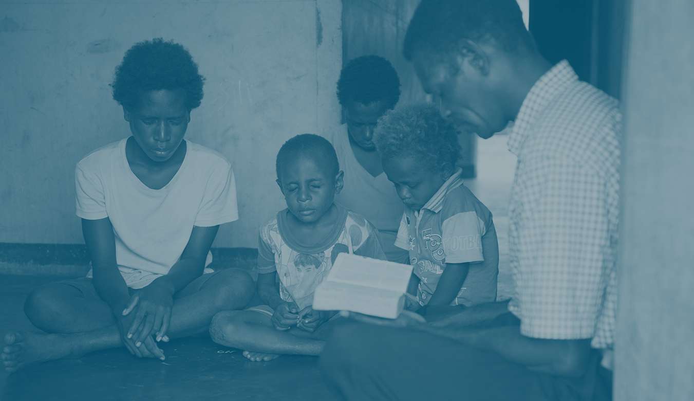 A family sitting in the floor with a Bible and praying together.