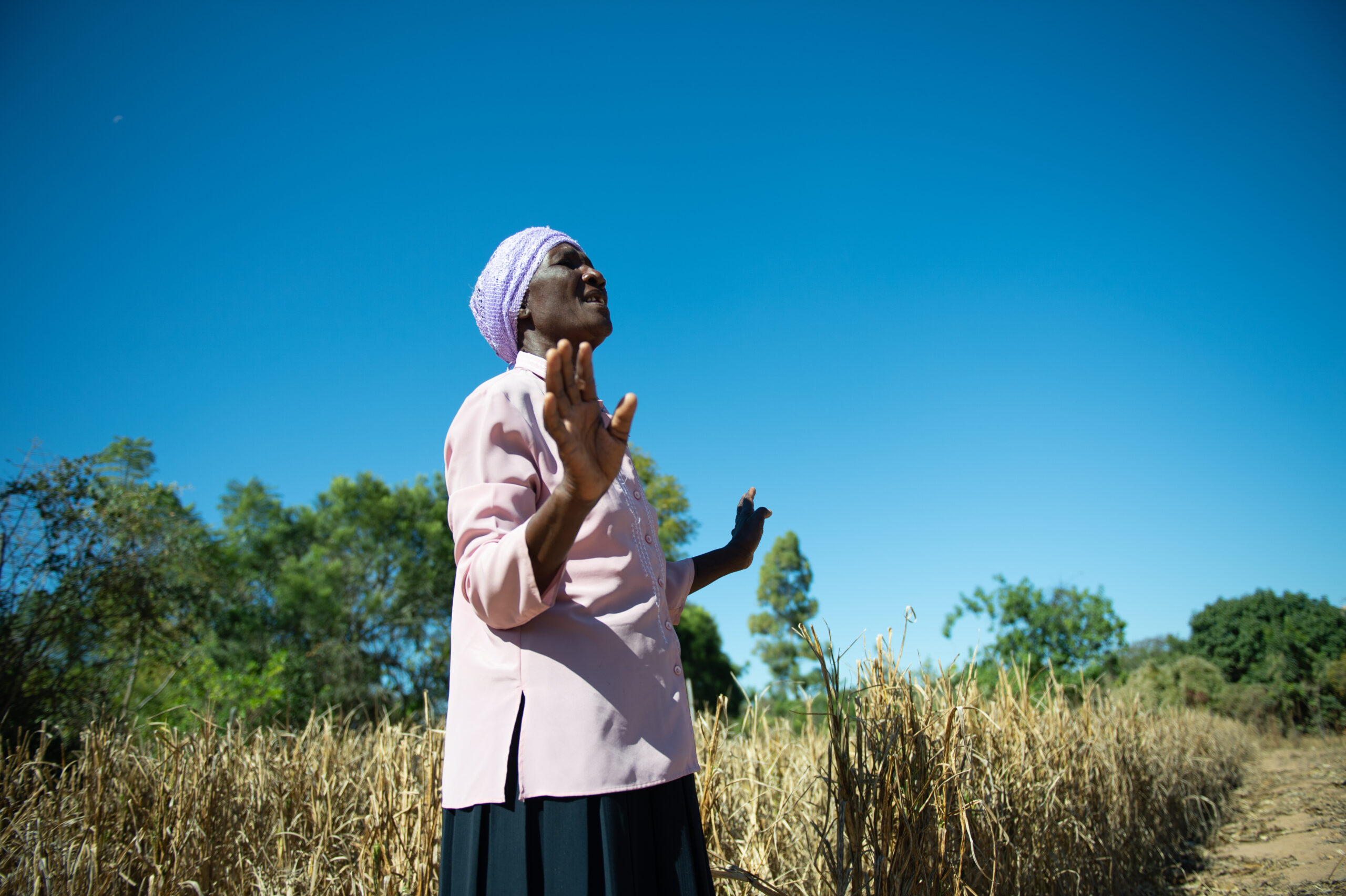 A lady raising her hands and signing in the middle of a field.