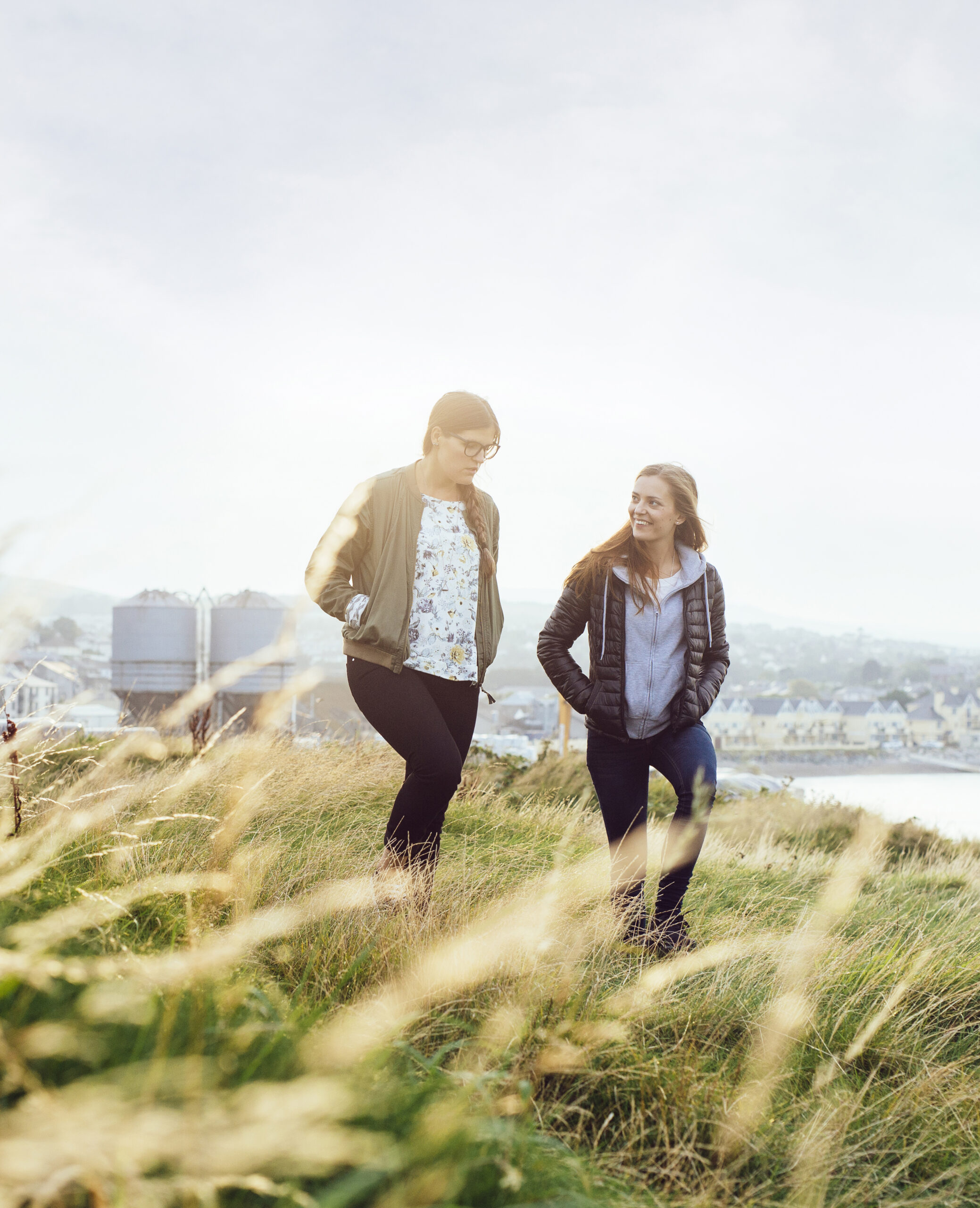 Two young ladies walking in a field talking.