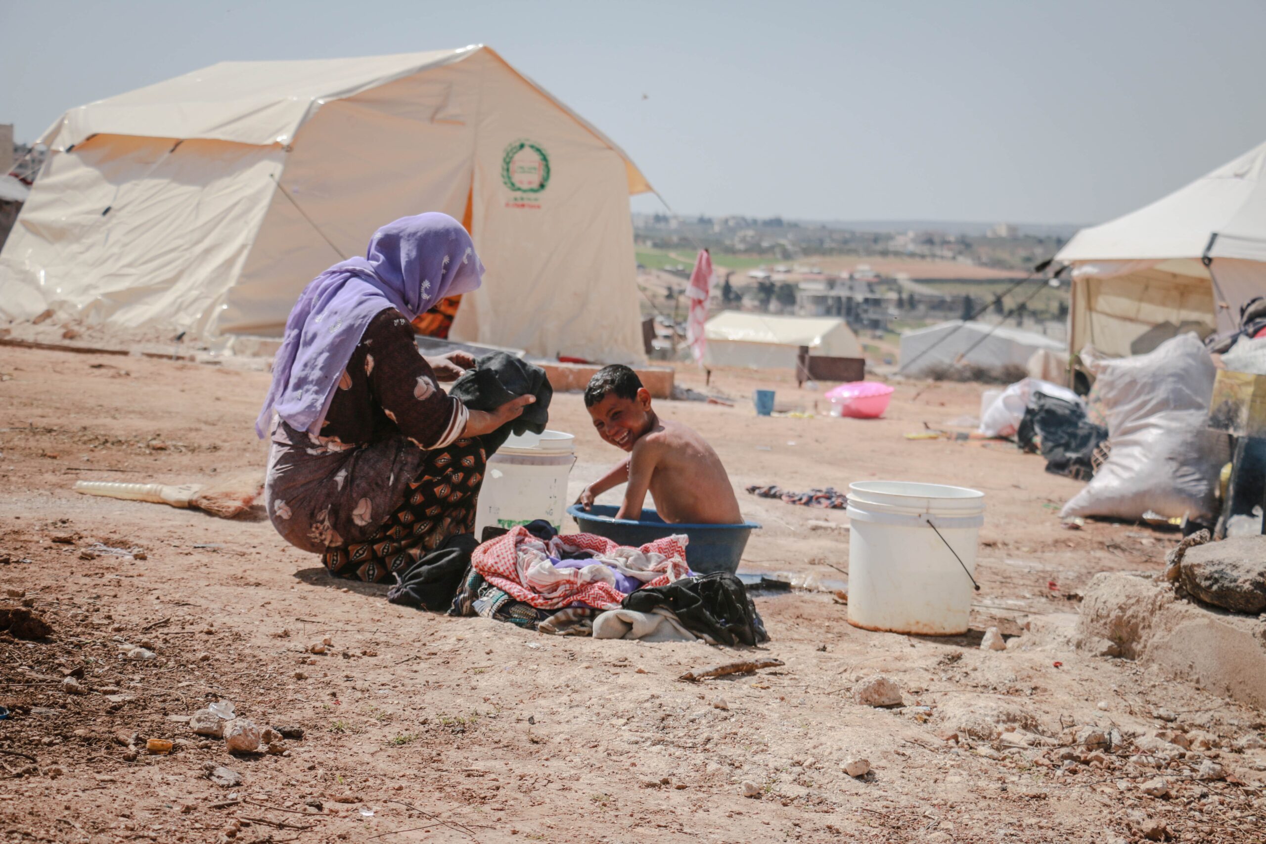 A woman gives a bath to her son in a bowl in a refugee camp.