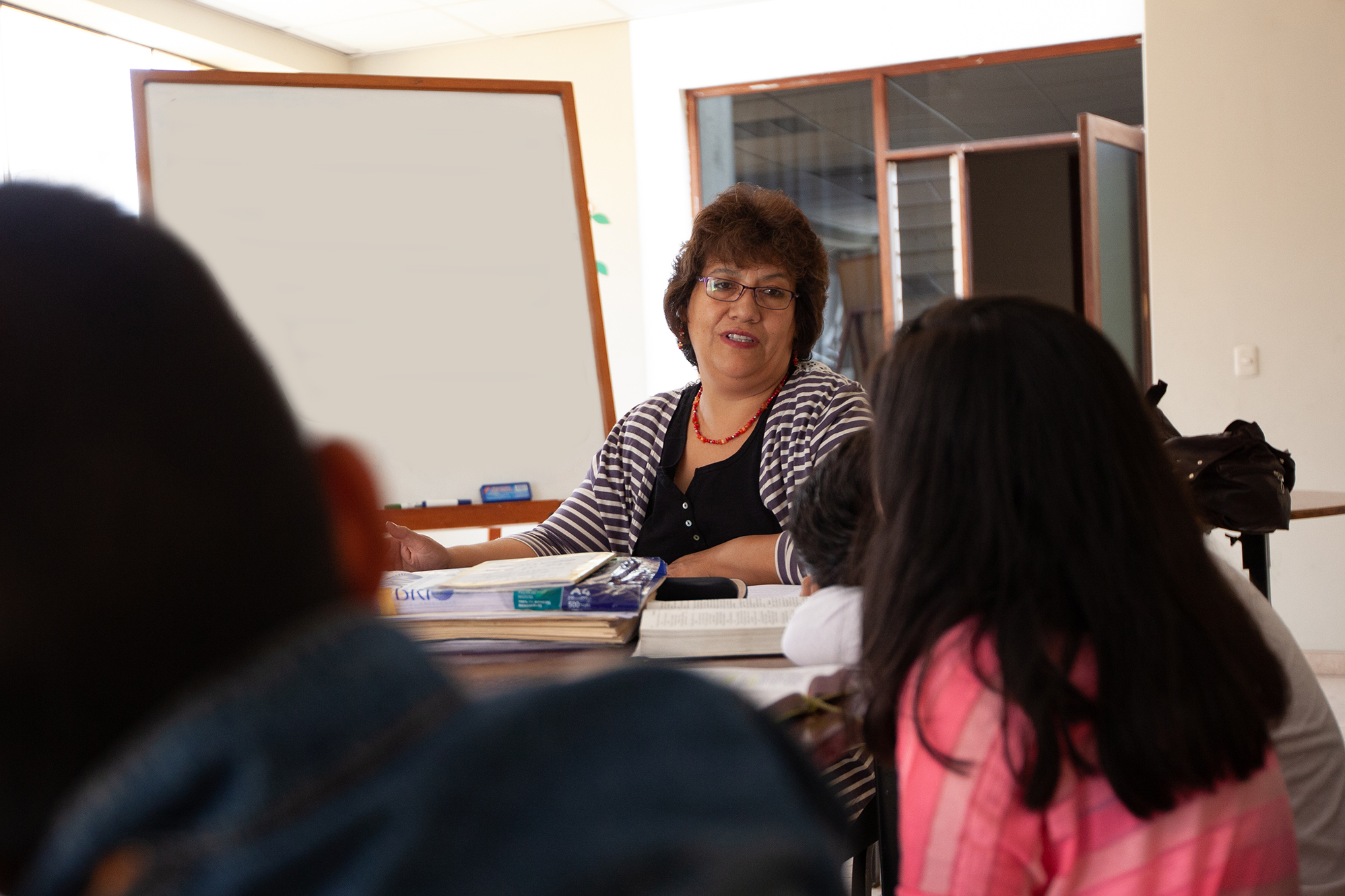 A lady sitting with students talking with Bibles open on the table.