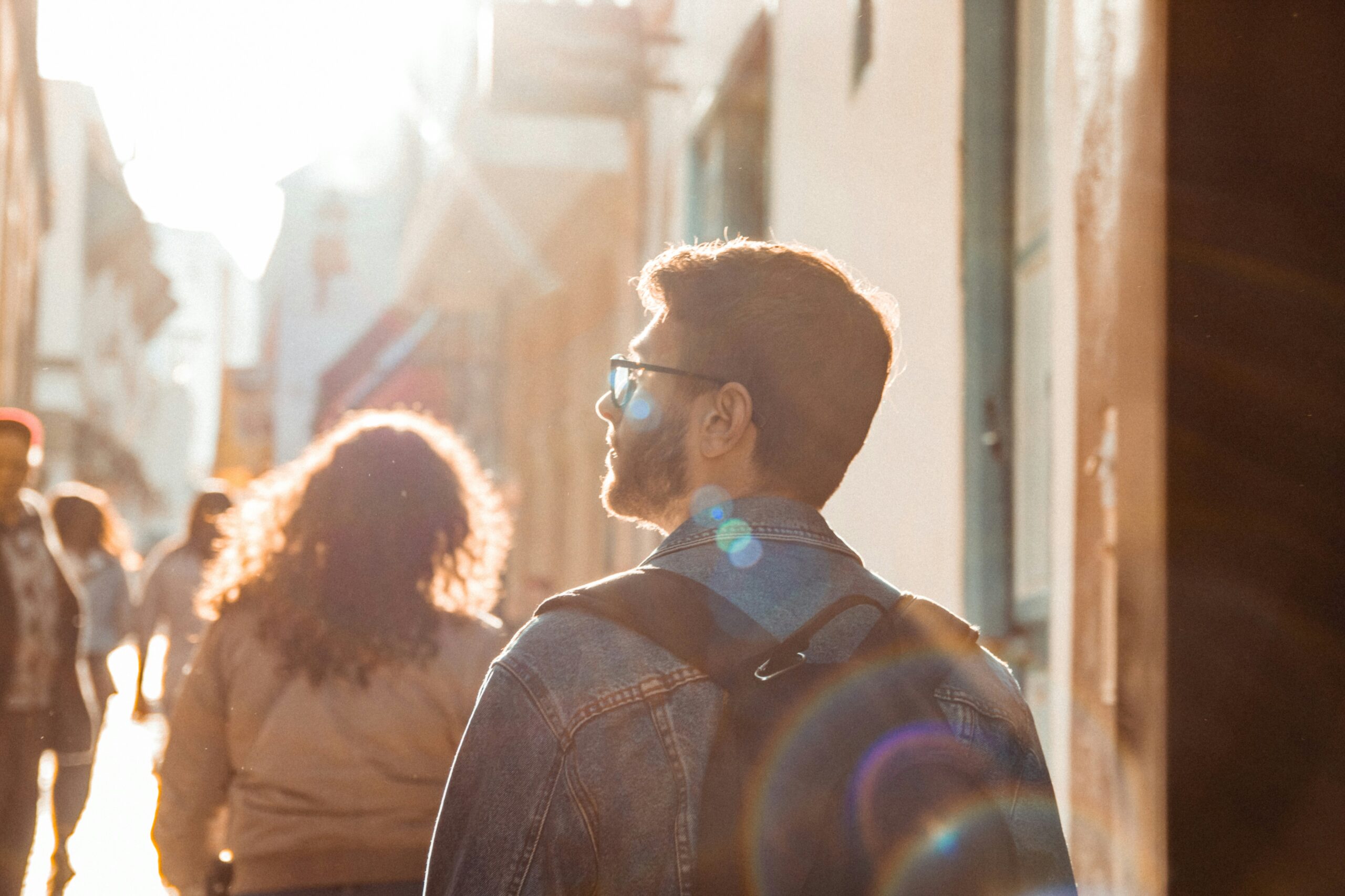 A man walking with a backpack through the city in the sunshine.